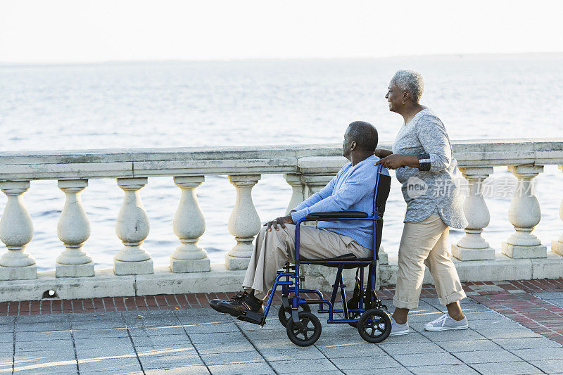一对老年夫妇，一个坐轮椅的男人，在海滨散步