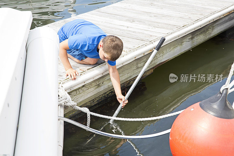 一个白人男孩在码头上用渔网捕鱼