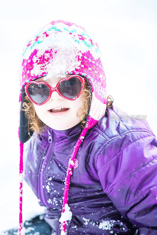 戴着心形太阳镜的小女孩在雪中玩耍