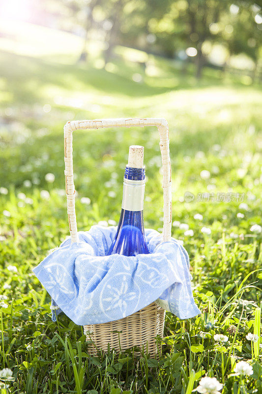 草地上的柳条篮子里放着酒瓶，准备夏天野餐。