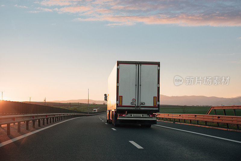 日落时分，一辆白色卡车行驶在两条车道的高速公路上