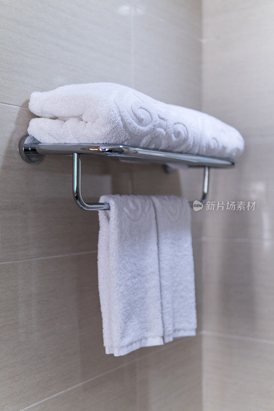 酒店浴室。折叠的白毛巾放在金属架上。
