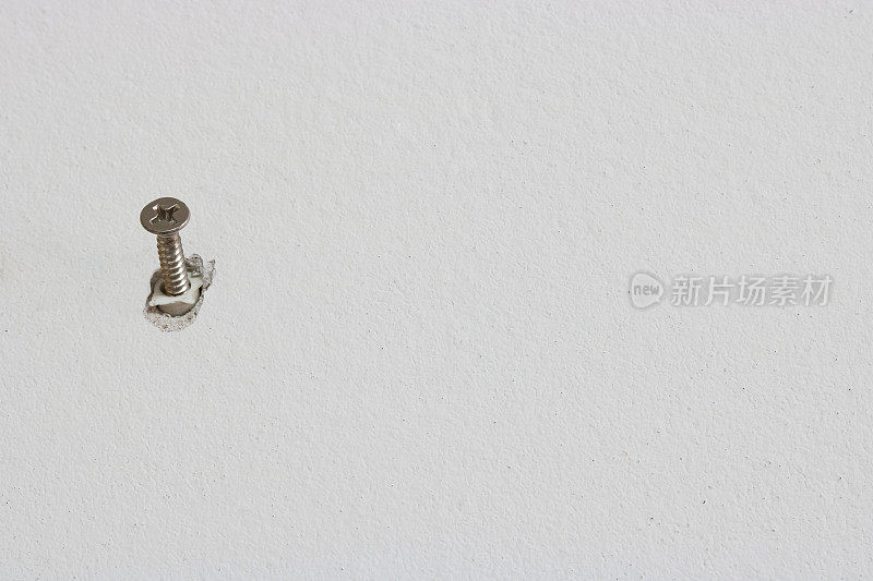 白色混凝土墙上的单颗螺丝钉，选择性聚焦