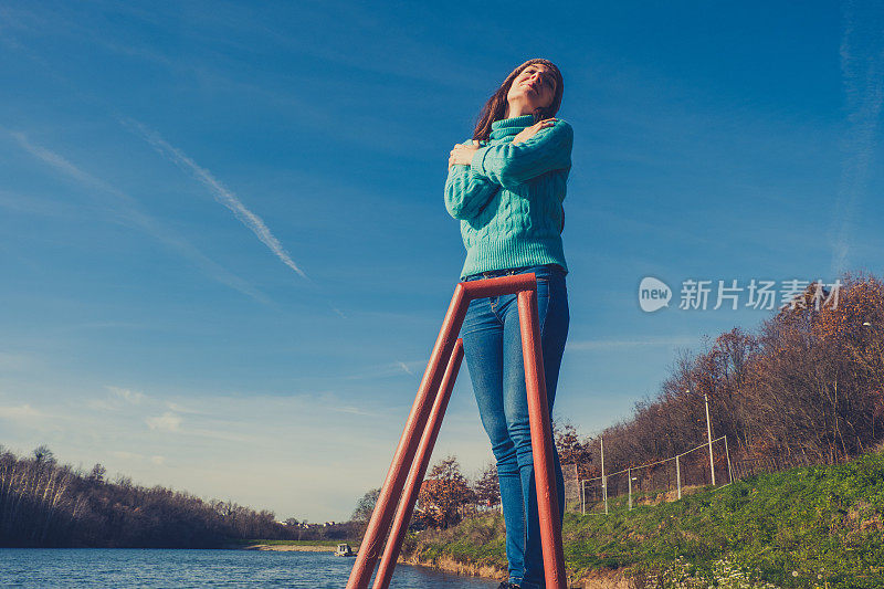 年轻女子躺在湖边的码头上，披着毯子，看日落