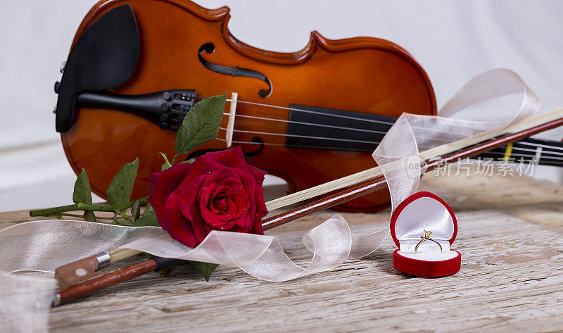 木桌上放着金戒指、红玫瑰和小提琴