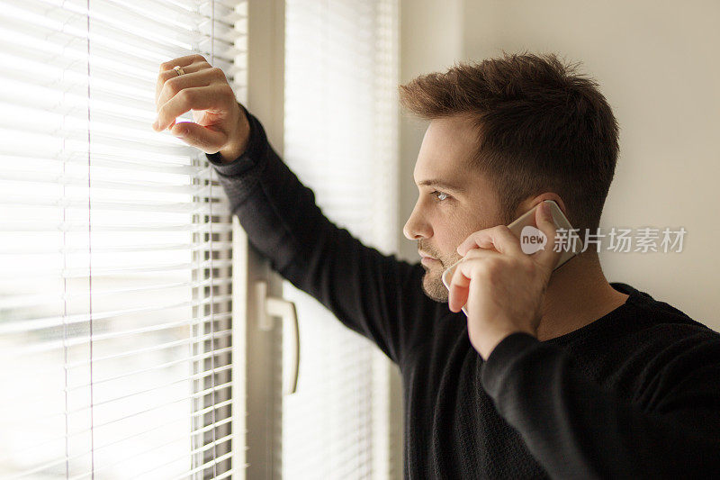 蓄着胡须的英俊男子站在窗前用智能手机