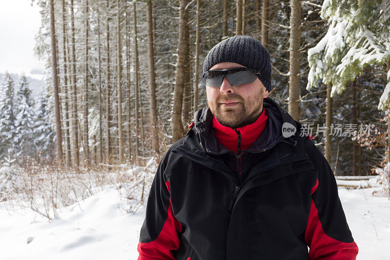 冬天的森林里，一个戴着墨镜的男人面带微笑