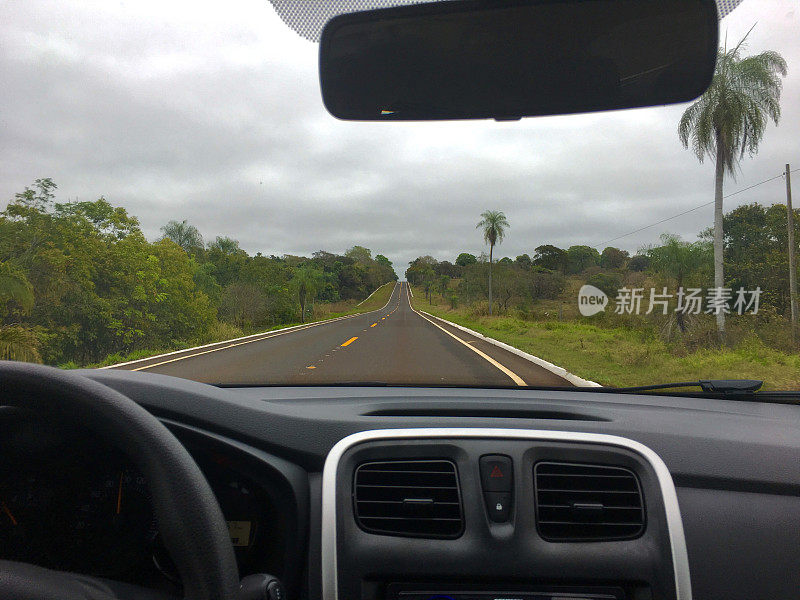 从两车道的乡村公路上看，里面有一辆紧凑型汽车，树木和天空