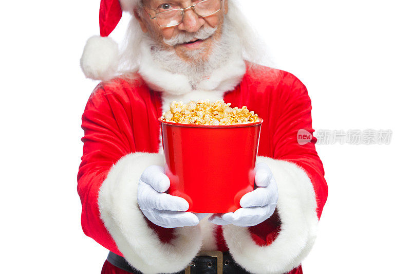 圣诞节。圣诞老人戴着白手套，双手捧着一桶爆米花，把它往前推，提出请客。参观电影院的概念，用爆米花看电影。孤立在白色背景上。