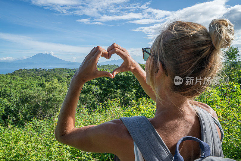 印尼巴厘岛阿贡火山上，一名年轻女子正在制作心形手指架。人们旅行热爱自然的概念