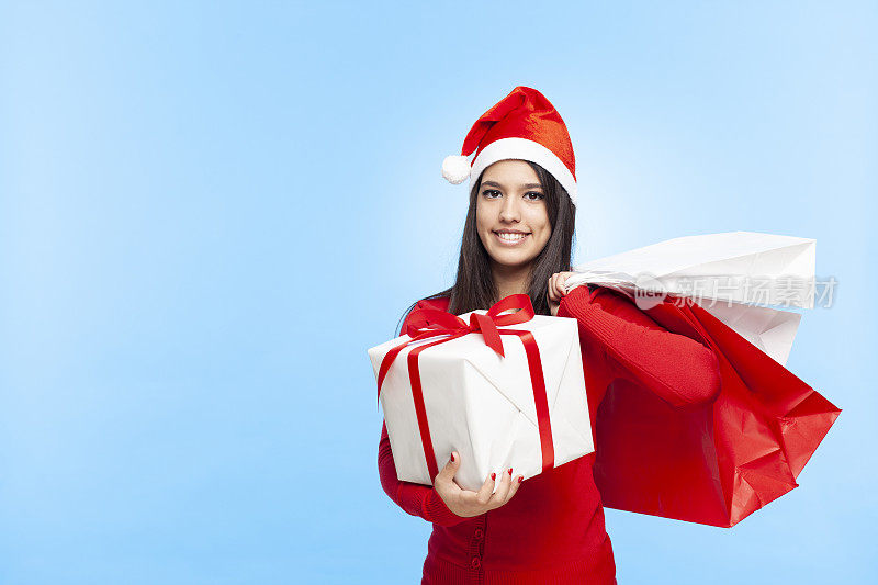 一个年轻快乐的女人戴着圣诞帽和圣诞购物礼物。