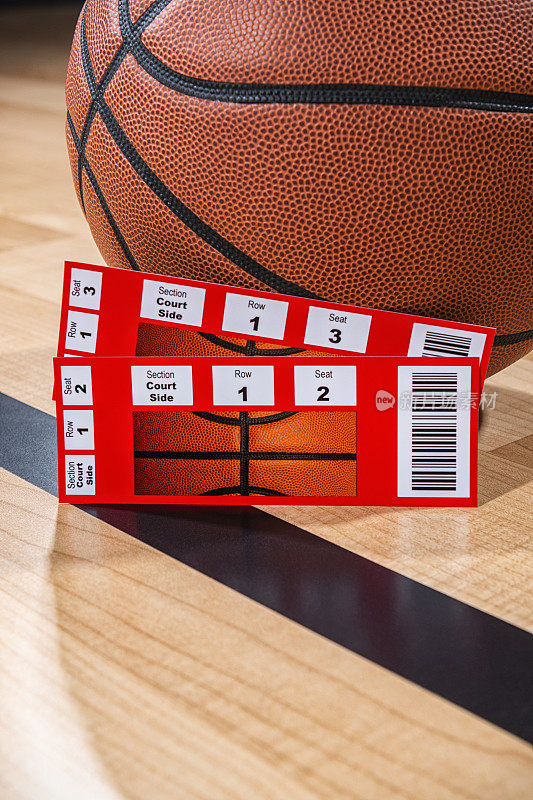 两张篮球票坐在一个球旁边，背景是竞技场的木地板