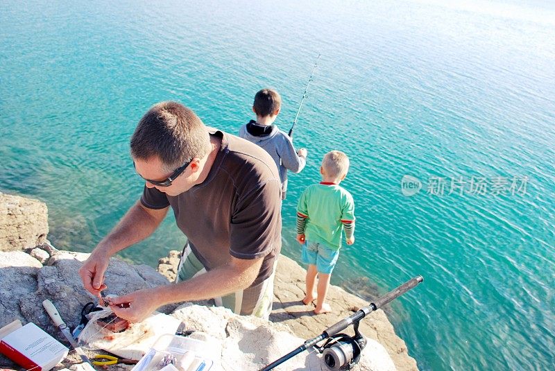 一个父亲和他的孩子们在海岸岩石上钓鱼