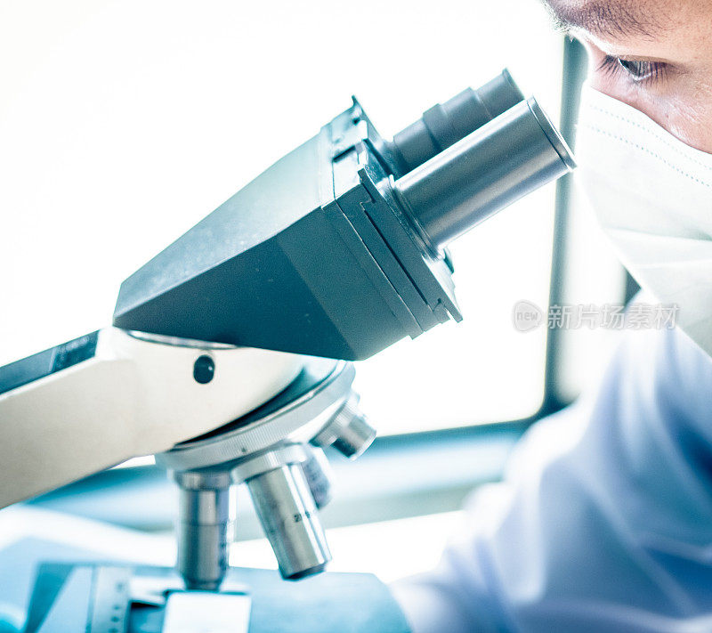 在实验室里透过显微镜观察的年轻科学家。年轻的科学家正在做一些研究。