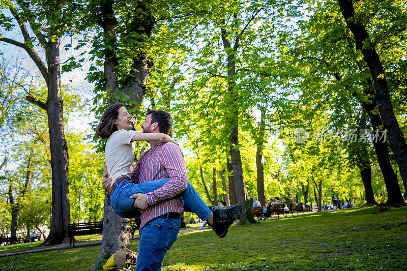纯粹的乐趣。这对年轻美丽的情侣在公园里散步时相依相偎。他们在一起的每一刻都更加相爱。年轻的情侣站在公园里微笑着拥抱。年轻美丽浪漫的情侣在公园里拥抱在一起。