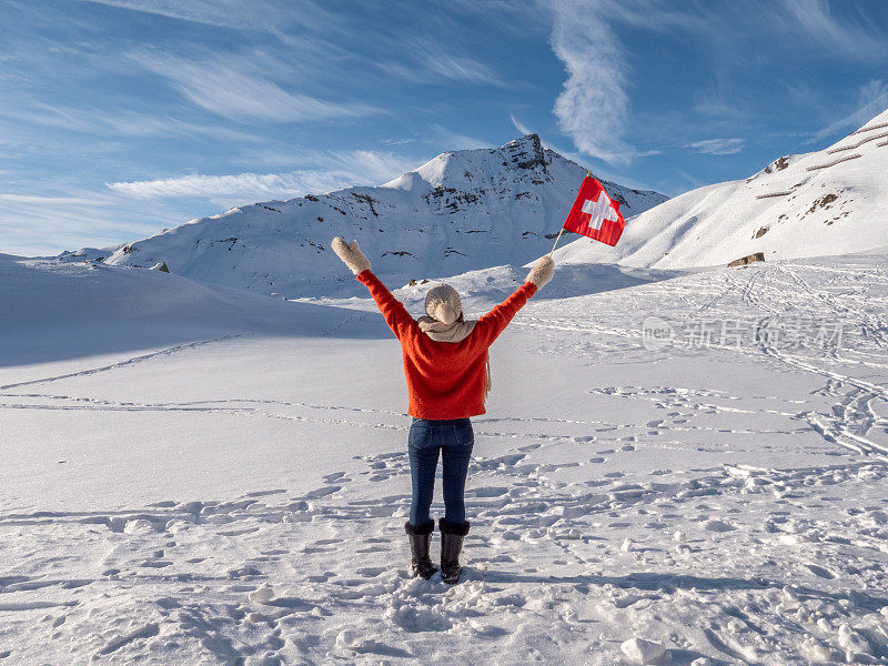 举着瑞士国旗站在瑞士阿尔卑斯山白雪皑皑的山上的女子