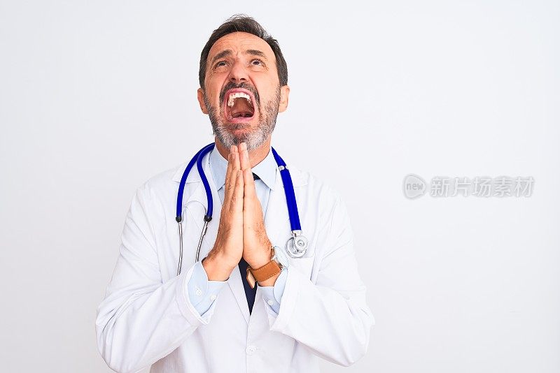 中年医生男子穿着大衣和听诊器站在孤立的白色背景乞求和祈祷与希望的表情在脸上非常情绪化和担忧。请求宽恕。宗教的概念。