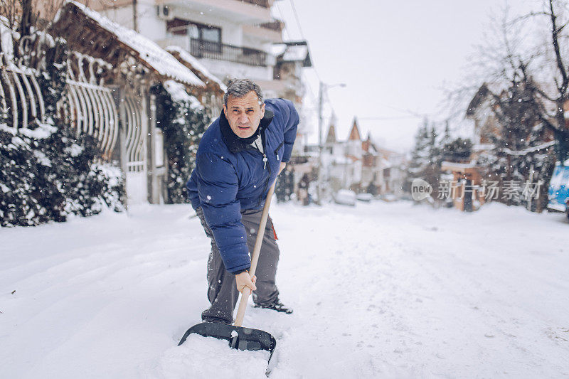 一个成熟的男人在清扫屋前的积雪