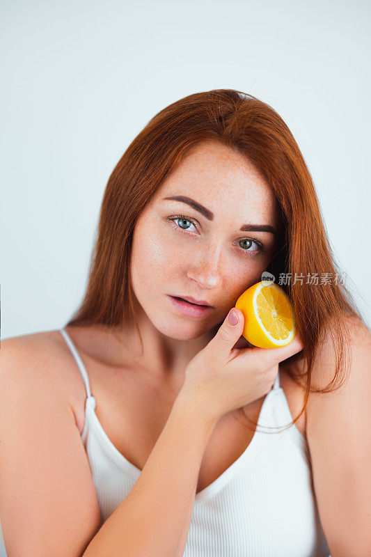 肖像红发年轻女子看起来感性站在孤立的白色背景拿着一半的橙色在她的脸附近，美丽肖像的概念