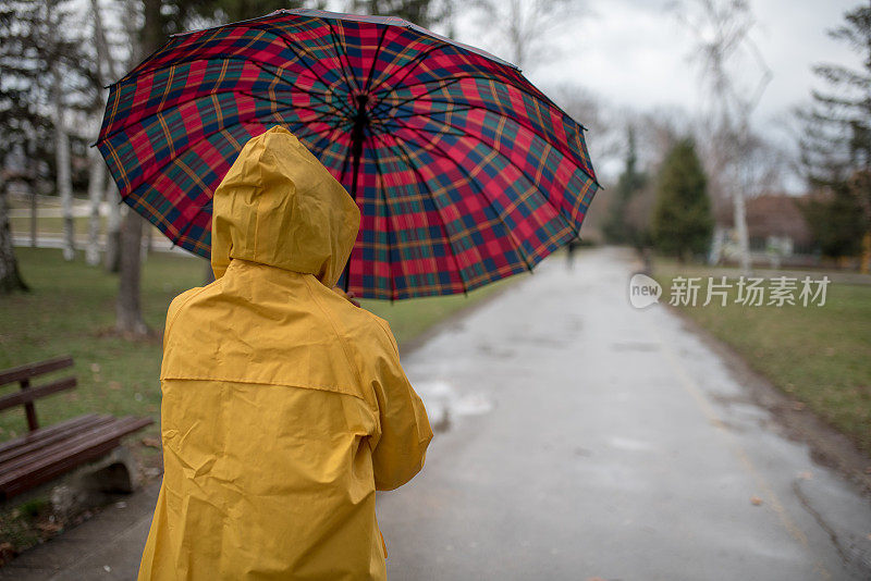 穿着黄色雨衣的年轻女子在公园里度过雨天