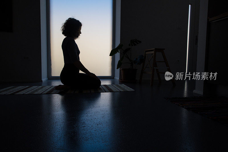 一个女人在家里做瑜伽的剪影，通过运动体现和意识