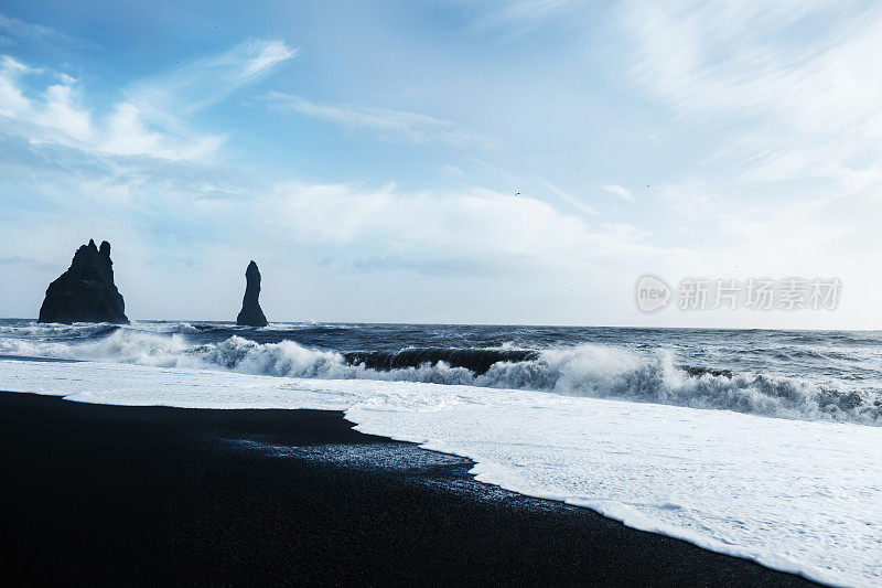 海滩景观的沉重的海浪冲击海岸上的黑色岩石的形成在远处。冰岛维克的黑沙滩