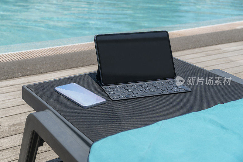 平板电脑智能键盘和手机在日光浴床上。