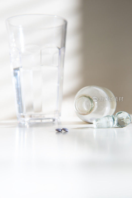两粒药丸放在一个别致的药瓶和一杯水旁边