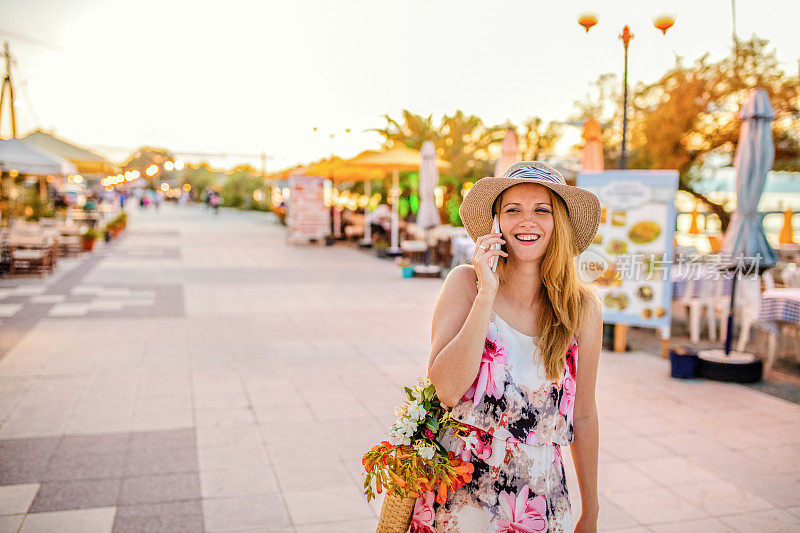微笑的女人挂在海滩上，用智能手机说话