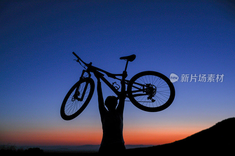 日出时，一个骑自行车的人把自行车举过头顶的剪影。