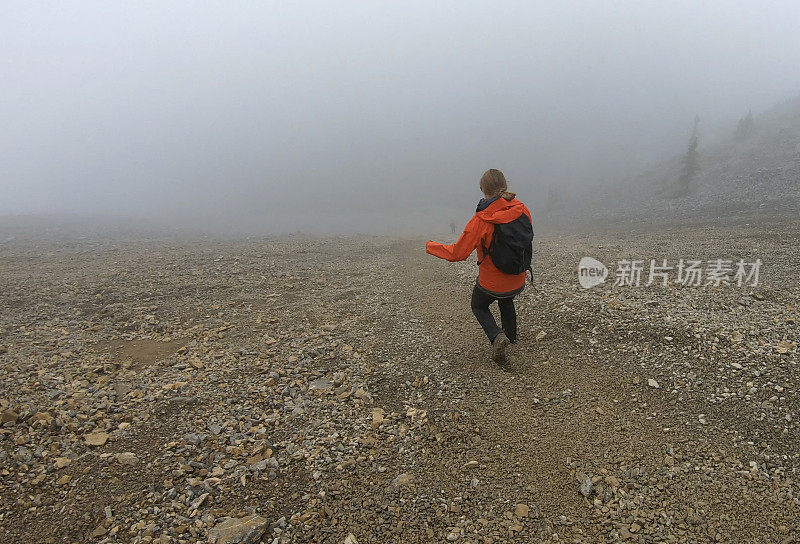 年轻的女登山运动员在雾中爬下一座山