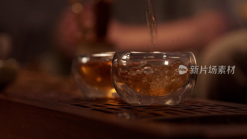 在中国的一个省，一个温馨的茶室。从一个瓷壶里涌出一股芬芳的茶，盛在两个玻璃碗里。特写,温暖的光。Slowmo