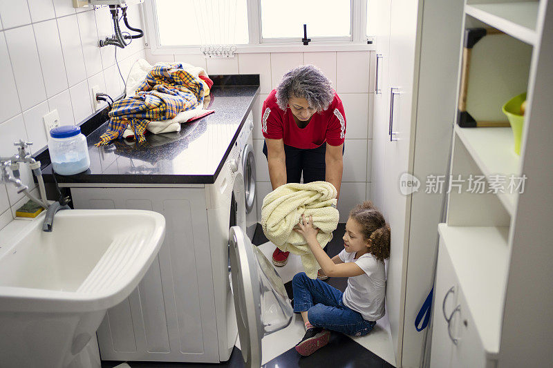 奶奶和孙女在洗衣房把脏衣服放进洗衣机里