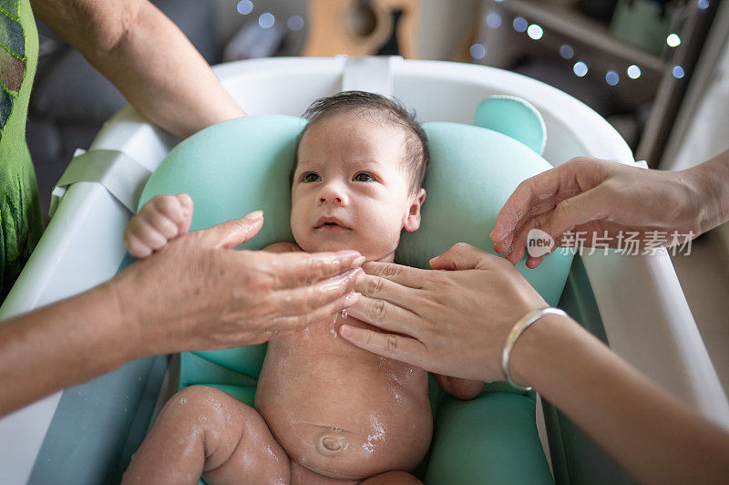 一名男婴在客厅的折叠式浴缸里与母亲和祖母一起洗澡