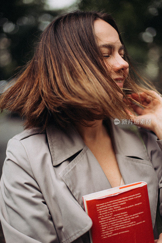 一个穿着风衣手上拿着红皮书的漂亮女人的肖像