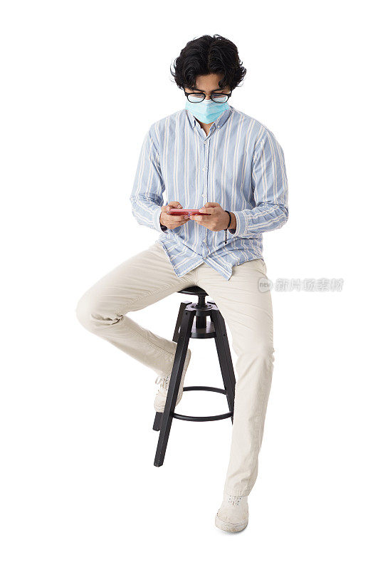 戴着口罩的男学生坐在凳子上用手机发短信
