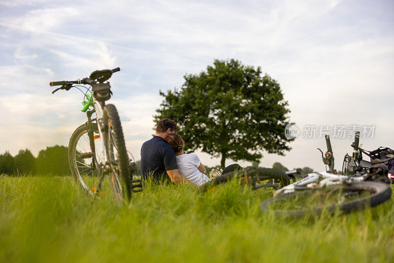 夏天，父母们骑完自行车正在草地上休息，他们坐在草地上拥抱，全家人骑的自行车在最前面