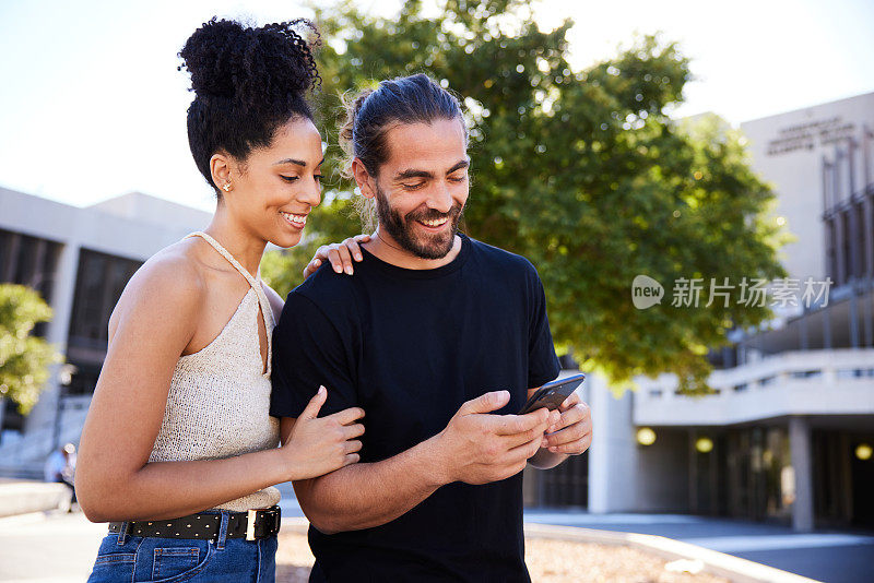 一对微笑的年轻夫妇在城里散步时看手机