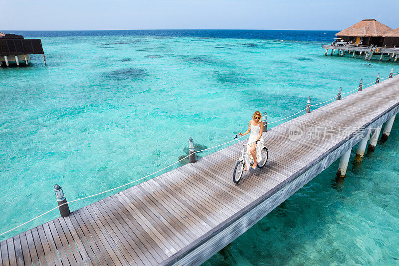 一名年轻女子骑着自行车在马尔代夫的木制码头上