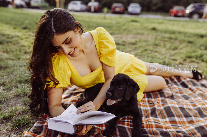 一位年轻女子一边看书一边和她的狗狗野餐