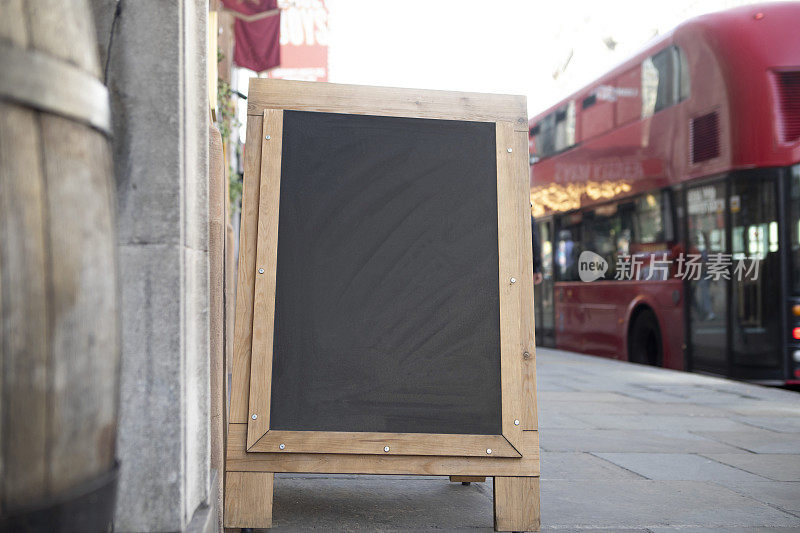 伦敦市中心人行道上的一块黑板，旁边是一辆红色公共汽车