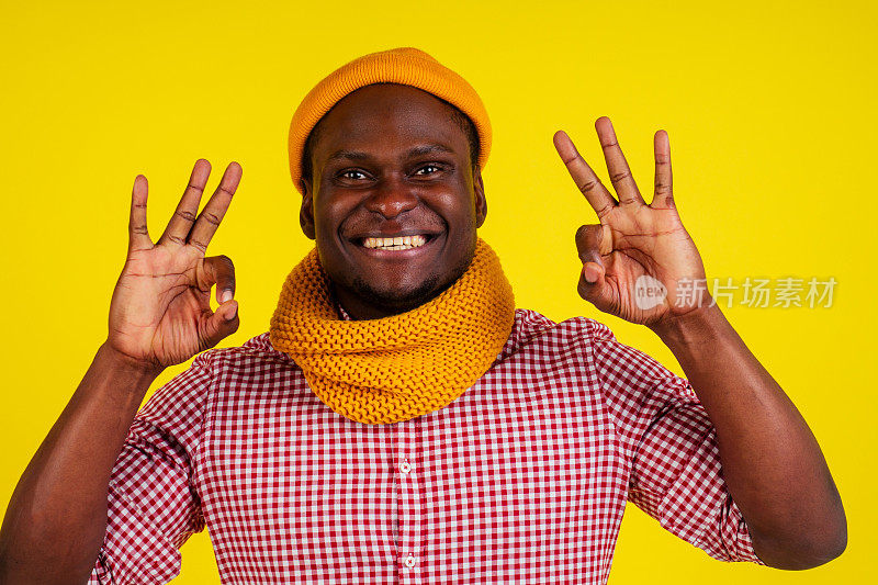 成功肖像迷人的非裔美国男子戴着针织帽和围巾，穿着红格子衬衫兴奋感觉好心情。秋春时装look套装显示okay姿态