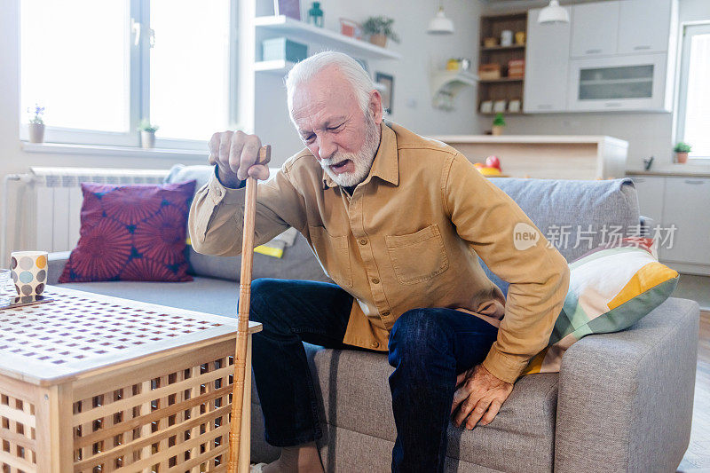一位身患残疾的大胡子老人独自一人在家里挣扎着起床，脸上露出了悲伤和绝望的表情。