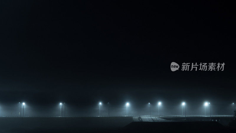 夜晚雾蒙蒙的高速公路被灯柱照亮。秋天雾蒙蒙的景观