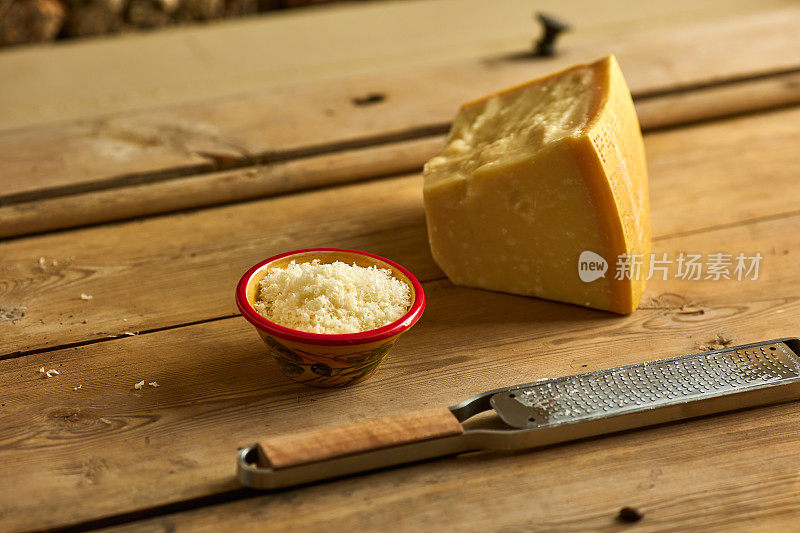 磨碎的奶酪在碗里，有块和磨碎器，放在木桌上