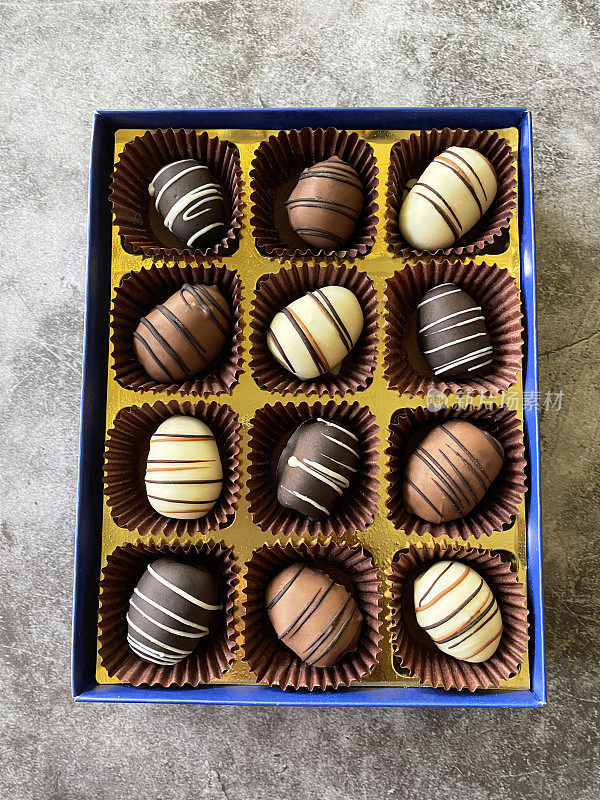 近距离图片，成排的个体，巧克力盒中覆盖着日期的巧克力，牛奶，纯巧克力和白巧克力，香草覆盖的干果，斑驳的灰色背景，高视图