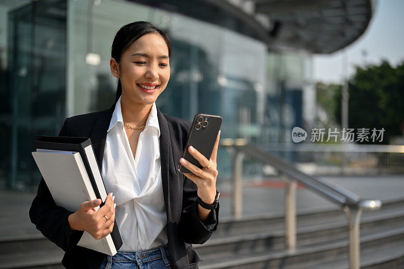 成功的亚洲女商人在街上走的时候用她的智能手机。