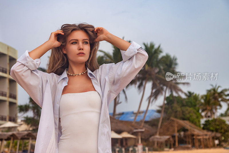 肖像快乐的漂亮年轻女子在白色衬衫在棕榈树背景沙滩上摆姿势。在热带海岸线享受轻松愉快的假期。旅游度假度假概念。复制文本空格