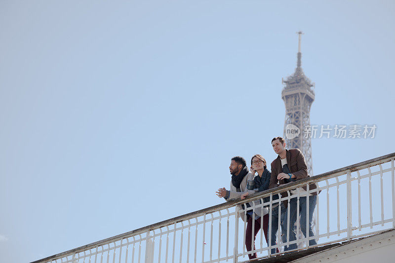 阳光明媚的法国巴黎，三个多民族的朋友站在塞纳河上的桥上，背景是埃菲尔铁塔