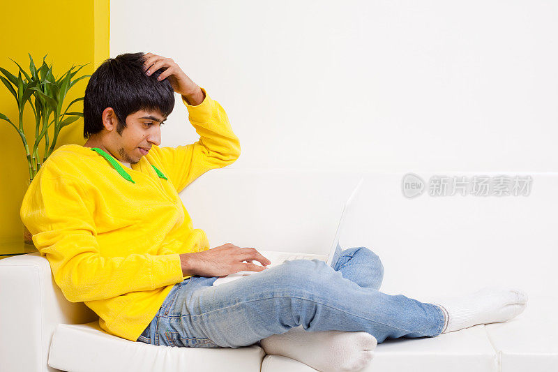年轻的印度少年愉快的笔记本电脑坐在沙发上